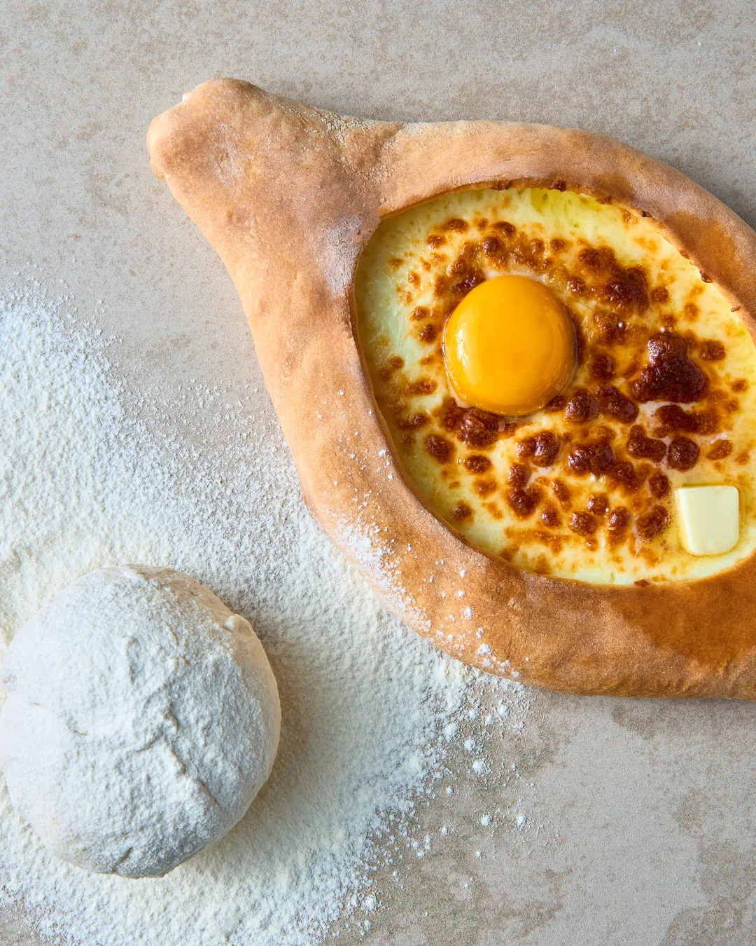 Adjarian khachapuri with egg, next to dough and flour